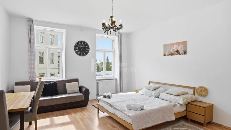 Helles Schlafzimmer mit Holzboden, Doppelbett, Sofa und Esstisch, ideal für Einzelpersonen oder Paare.