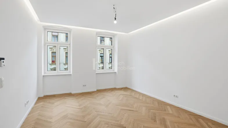 Helles Zimmer mit Fischgrätparkettboden, weißen Wänden und modernen Deckenleuchten.