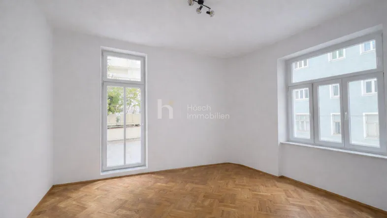 Helles Zimmer mit Fischgrätparkett und zwei großen Fenstern, bereit zur individuellen Gestaltung.