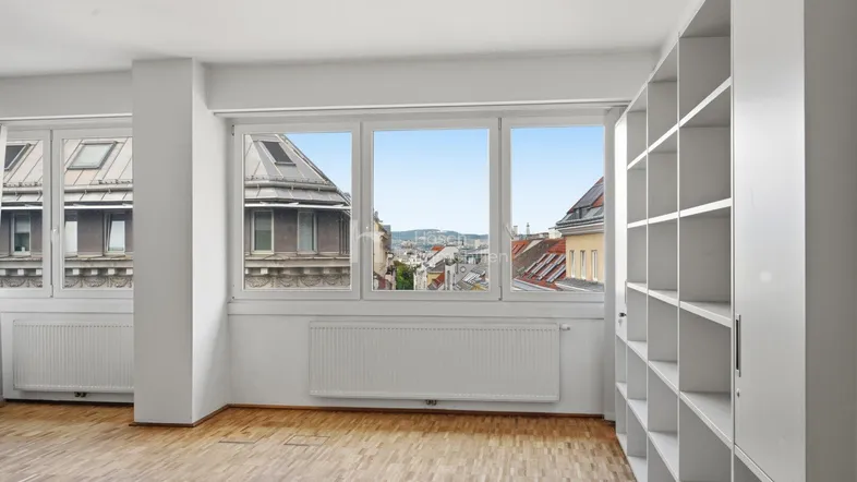 Helles Zimmer mit Parkettboden, Einbauregalen und weitem Blick über die Stadt.