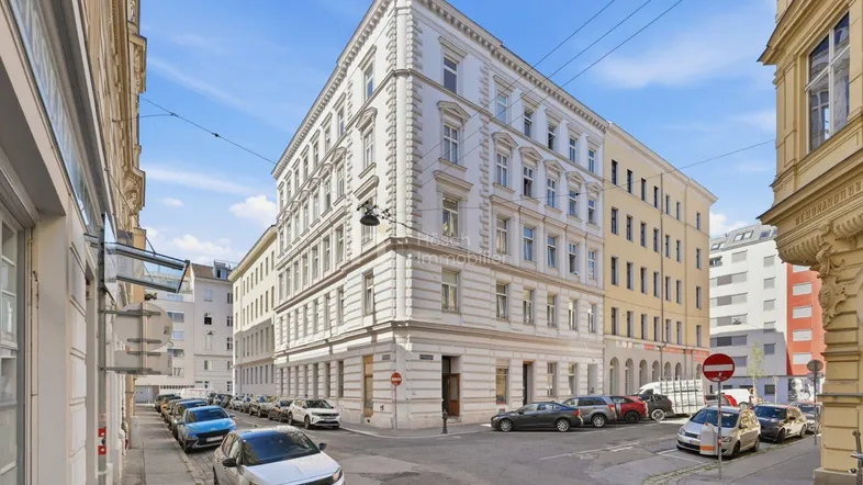 Historisches Eckgebäude in der Stadt mit klassischer Architektur und geparkten Autos auf der Straße.