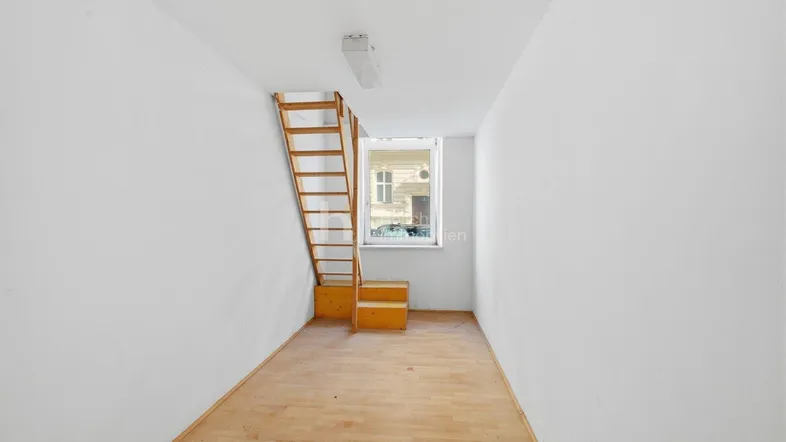 Leerer Raum mit Holzleiter und Fenster, bereit für die Renovierung und individuelle Gestaltung.