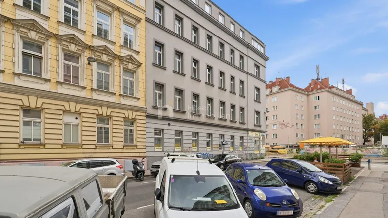 Mehrere Gebäude entlang einer Straße mit geparkten Autos unter blauem Himmel.