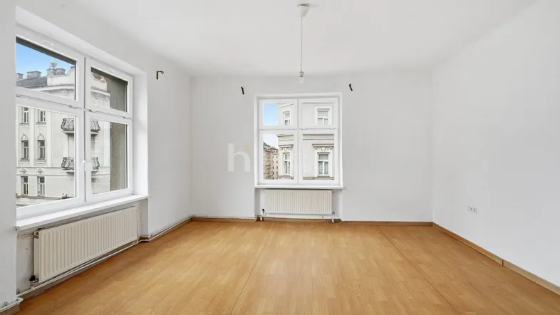 Helles, leeres Zimmer mit Parkettboden und großen Fenstern, die auf die Straße blicken.