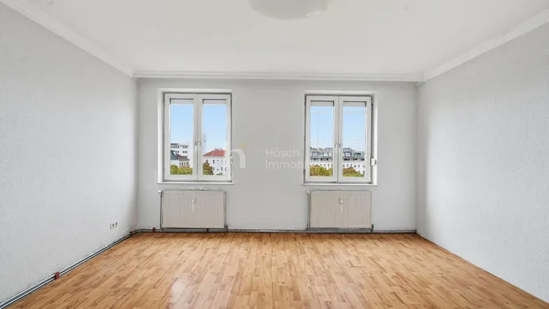 Helles Zimmer mit Parkettboden und zwei Fenstern, die einen Blick auf die Stadt bieten.