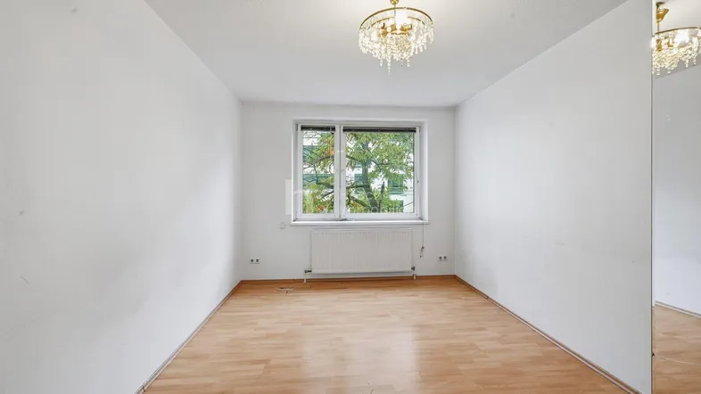 Helles Zimmer mit Laminatboden, Kronleuchter und Blick ins Grüne.