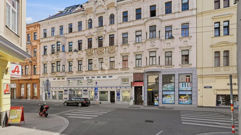 Historisches Mehrfamilienhaus an einer belebten Straße mit Geschäften im Erdgeschoss.