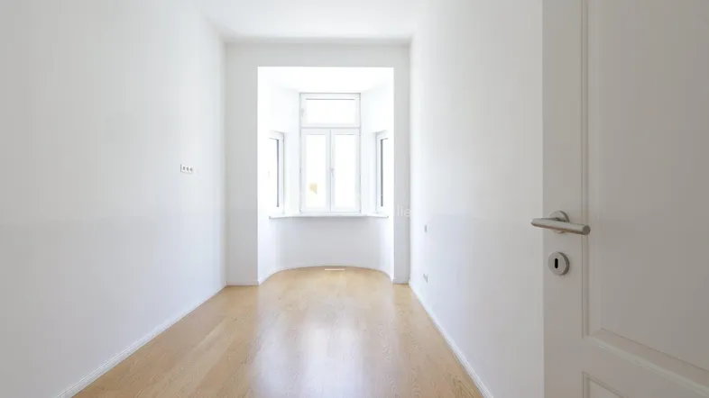 Helles Zimmer mit Erkerfenster und hellem Parkettboden, ideal als Wohn- oder Schlafzimmer.