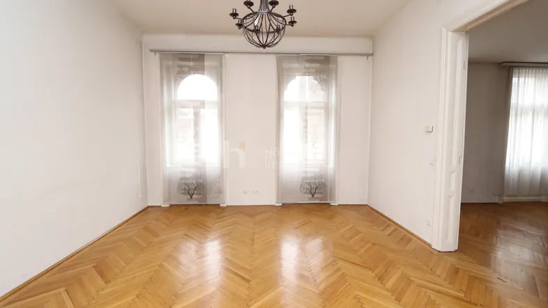 Helles Zimmer mit Fischgrätparkettboden, weißen Wänden und einem eleganten Kronleuchter.
