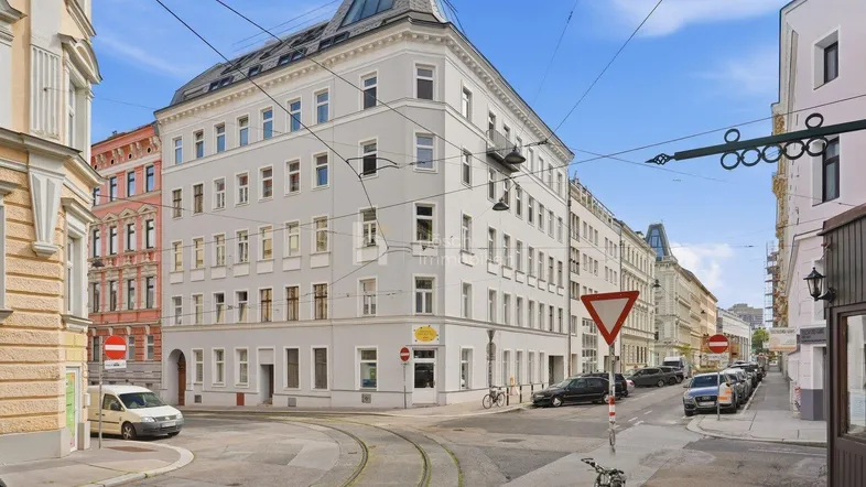Historisches Eckgebäude mit klassischer Architektur und Mansarddach in urbaner Umgebung.