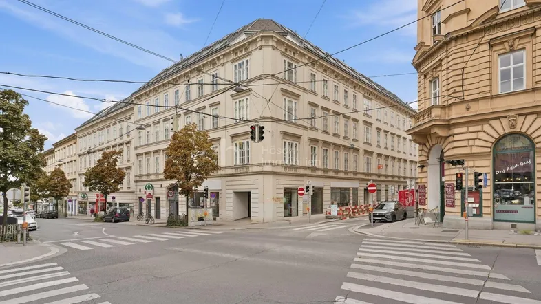 Großes Eckgebäude in urbaner Umgebung mit klassischer Architektur und Geschäften im Erdgeschoss.