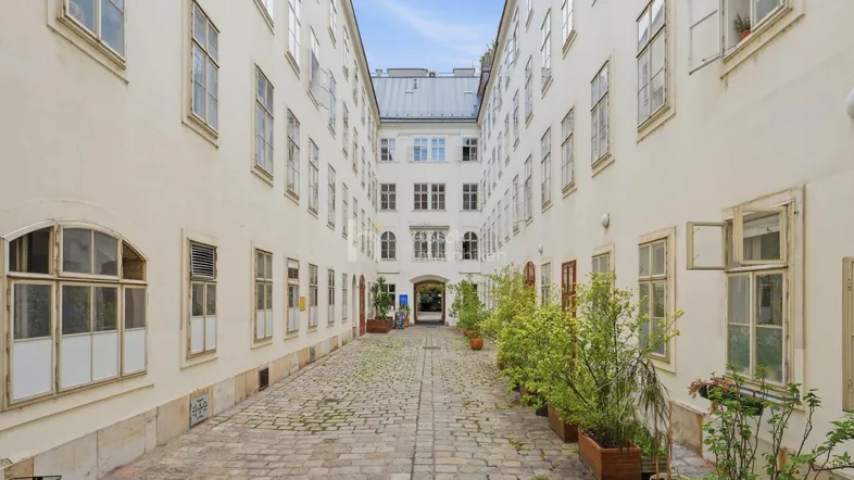 Historischer Innenhof eines Gebäudes mit Kopfsteinpflaster und begrünten Pflanzenkübeln, der eine ruhige Atmosphäre schafft.