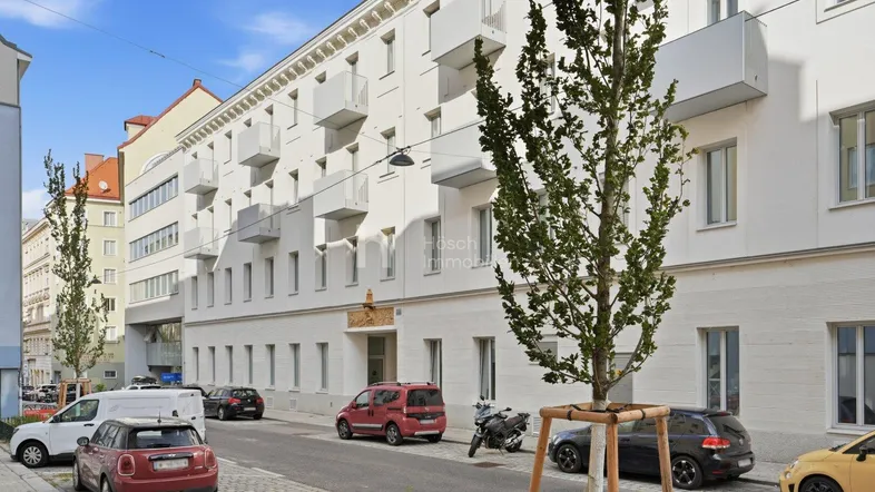 Moderne Wohngebäude-Fassade mit zahlreichen Balkonen und parkenden Autos auf der Straße.