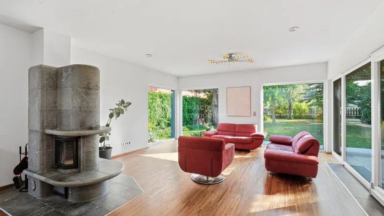 Helles Wohnzimmer mit modernem Kamin, roten Sofas und großen Fenstern zum Garten.