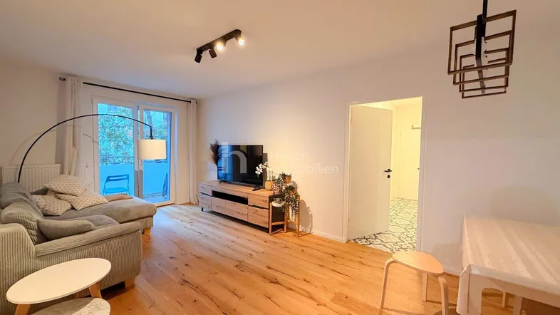 Helles Wohn- und Esszimmer mit Holzboden, gemütlichem Sofa und Zugang zum Balkon.