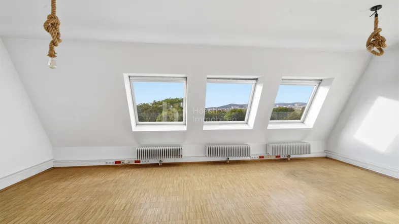 Helles Dachzimmer mit drei Dachfenstern, Holzboden und schrägen Wänden, bereit zur Einrichtung.
