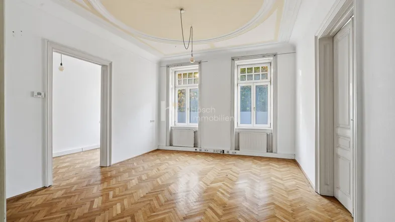 Helles Zimmer mit Fischgrätparkett und Stuckdecke in einem Altbau.