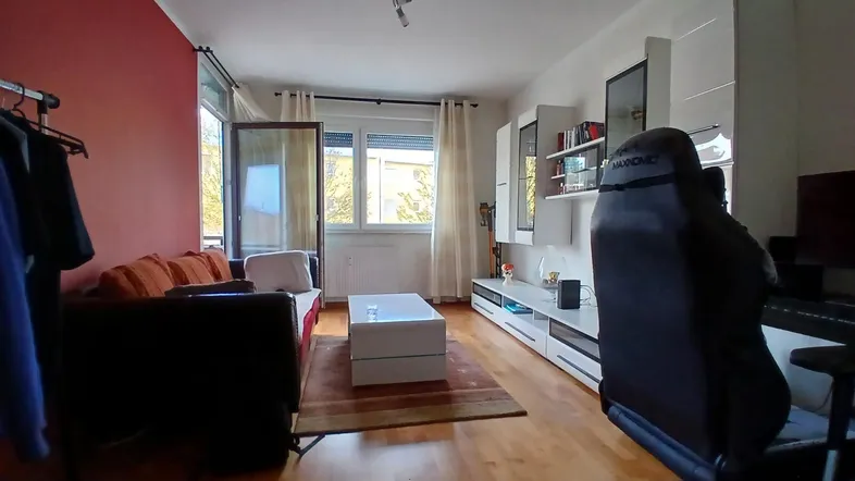 Helles Wohnzimmer mit Holzboden, roter Akzentwand und modernem Medienmöbel. Große Fenster lassen viel Licht herein.