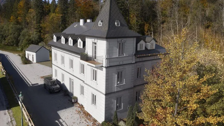 Historische Villa mit markantem Turm, umgeben von herbstlicher Landschaft und Bäumen in voller Farbe.