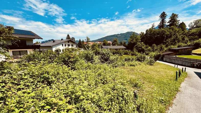 Unbebautes Grundstück mit umliegenden Wohnhäusern und grüner Landschaft unter blauem Himmel.