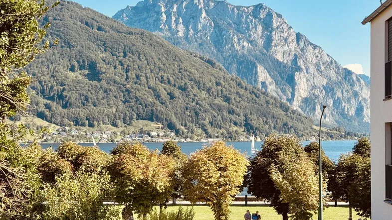 Panoramablick auf den See und die Berge, umgeben von üppiger grüner Landschaft und Bäumen.