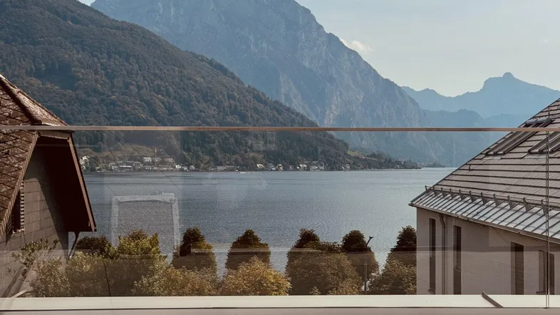 Panoramablick von der Terrasse auf den See und die umliegenden Berge mit moderner Glasbrüstung.