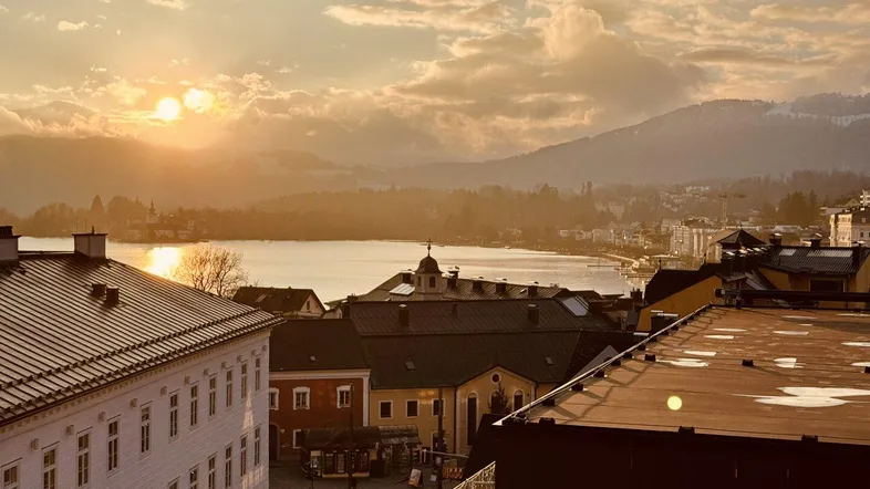Sonnenuntergang über einer Stadt mit See und Bergen im Hintergrund, von einem Dach aus gesehen.