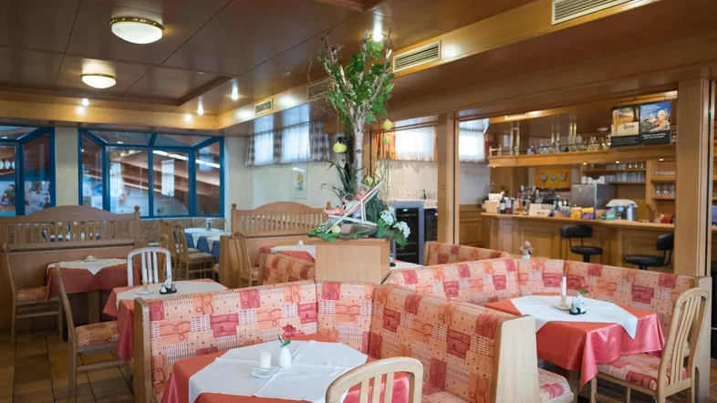 Gemütlicher Restaurantbereich mit Holztäfelung, gepolsterten Sitzbänken und Tischen mit roten Tischdecken.