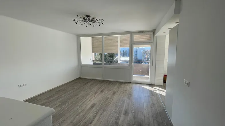 Helles Wohnzimmer mit modernem Laminatboden, weißen Wänden und Zugang zu einem sonnigen Balkon.