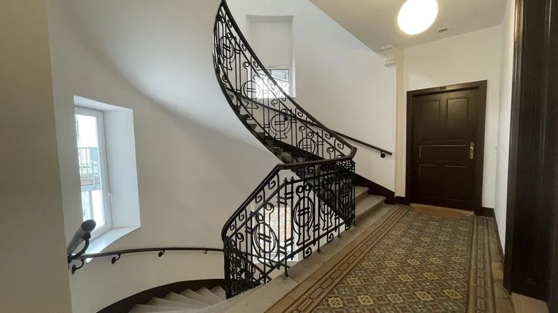 Eindrucksvolles Treppenhaus mit kunstvollem schmiedeeisernem Geländer und gemusterten Fliesenböden in einem Altbau.