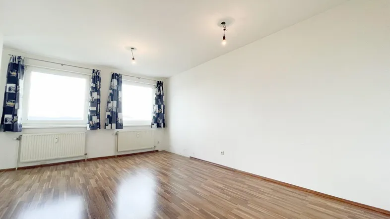 Helles, leeres Zimmer mit Parkettboden und zwei Fenstern, bereit zur individuellen Gestaltung.