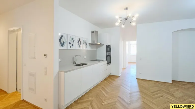 Moderne Küche mit weißen Schränken, heller Arbeitsplatte und Fischgrätparkett in einem offenen Wohnbereich.