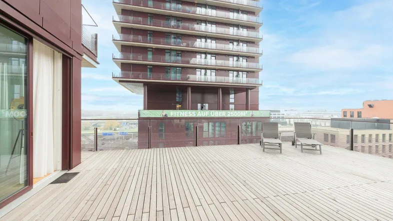 Große Holzterrasse mit Liegestühlen und Blick auf das moderne Hochhaus und die Umgebung.