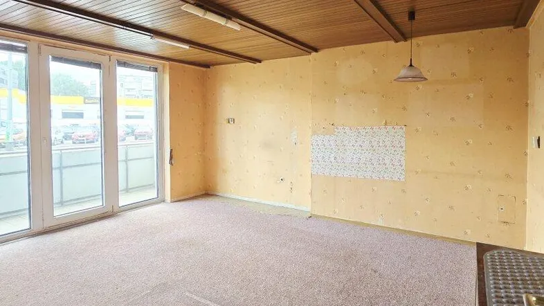 Geräumiger Innenraum mit Teppichboden, Holzdecke und Zugang zu einem Balkon.