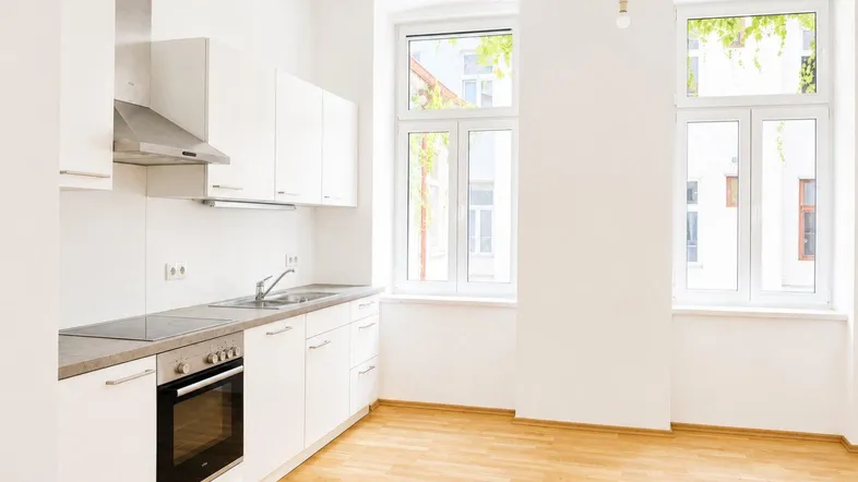 Helle Einbauküche mit weißen Schränken, integrierten Geräten und Laminatboden.