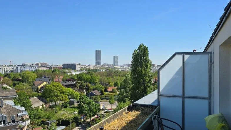 Balkon mit Sitzgelegenheiten und weitem Blick über die Stadtlandschaft und entfernte Gebäude.