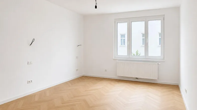 Helles, leeres Zimmer mit Fischgrätparkett und großem Fenster, bereit zur individuellen Gestaltung.