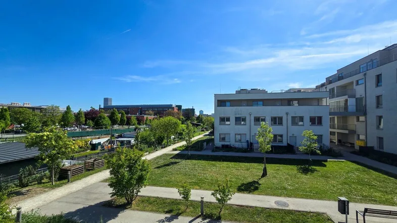Weitläufige Grünflächen und moderne Wohngebäude unter strahlend blauem Himmel in der Umgebung.
