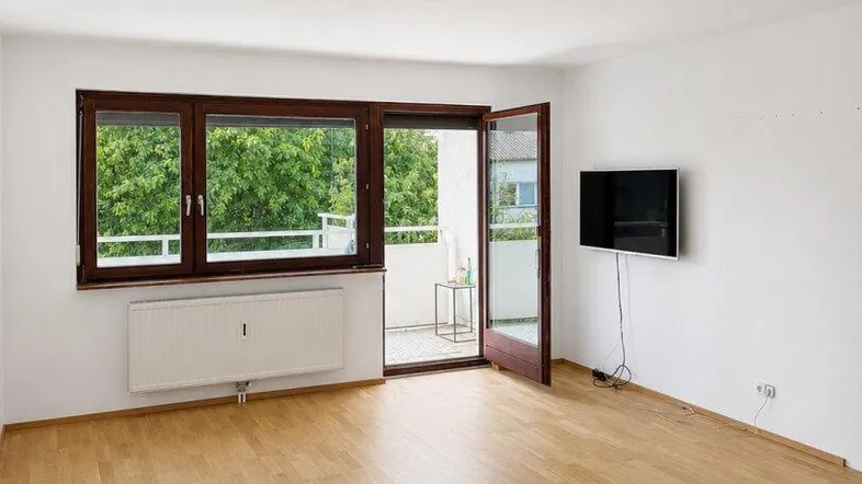 Helles Wohnzimmer mit Parkettboden, weiß gestrichenen Wänden und Zugang zum Balkon.