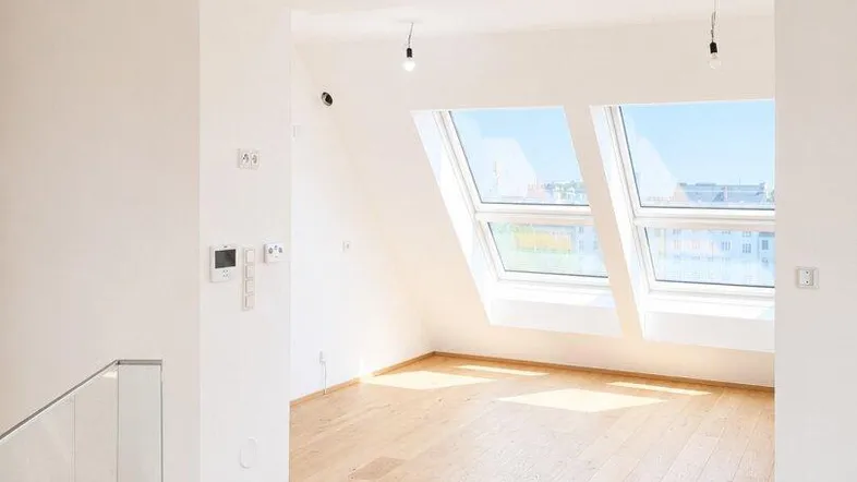 Heller, leerer Raum im Dachgeschoss mit großen Dachfenstern und Holzfußboden.
