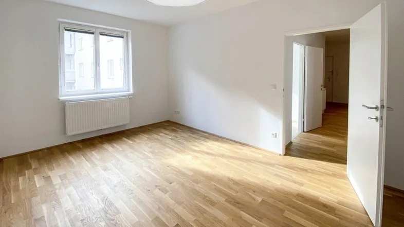 Heller, leerer Raum mit Parkettboden, weißen Wänden und Fenster, bereit zur individuellen Gestaltung.