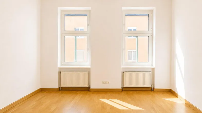 Helles Zimmer mit Holzboden und zwei Fenstern, ideal als Wohn- oder Schlafbereich nutzbar.