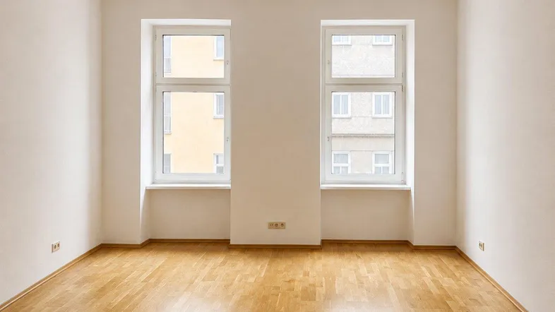 Helles Zimmer mit Parkettboden und zwei Fenstern, bereit zur individuellen Gestaltung.