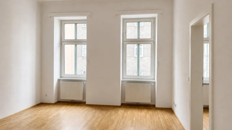 Helles, leeres Zimmer mit Parkettboden und zwei großen Fenstern, bereit zur individuellen Gestaltung.