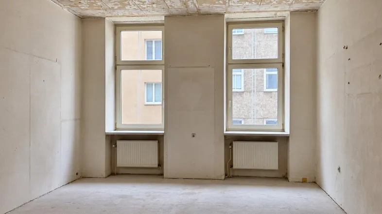 Unrenovierter Raum mit abblätternder Decke und zwei Fenstern, bereit für die Sanierung.