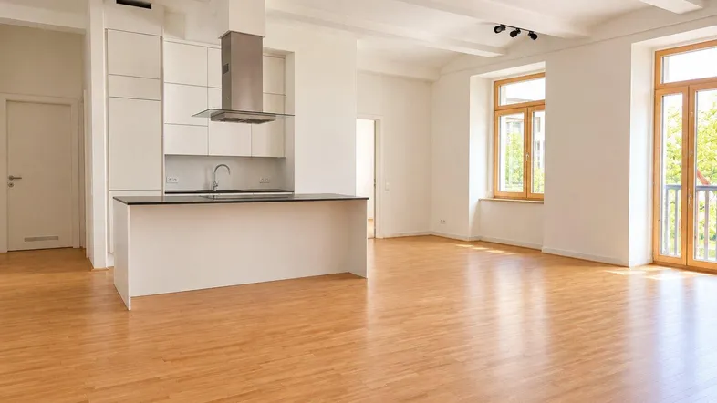 Heller, offener Wohnbereich mit moderner Einbauküche, Holzboden und Zugang zu einem Balkon.