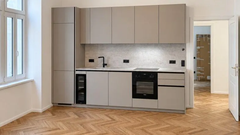 Moderne Küche mit grauen Schränken, integrierten Geräten und Fischgrätparkett in einem hellen Raum.