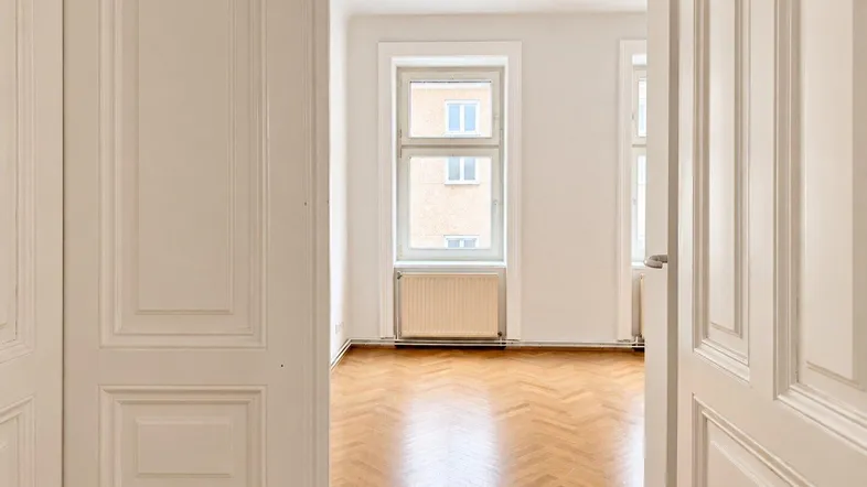 Helles Zimmer mit Fischgrätparkett und Blick auf die umliegenden Gebäude.