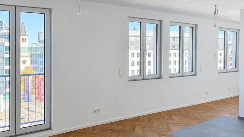 Helles Zimmer mit Fischgrätparkett, weißen Wänden und Zugang zu einem französischen Balkon mit Stadtblick.