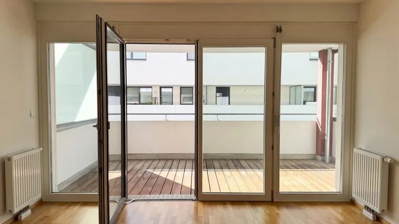 Geräumiges Zimmer mit Holzboden und breiter Fensterfront, die viel Tageslicht hereinlässt.